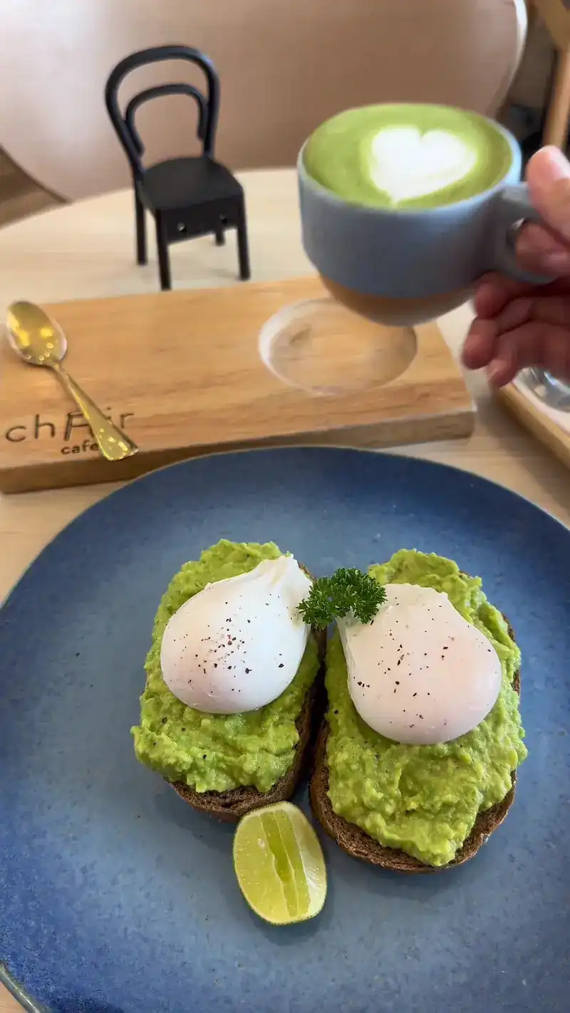 Avocado toast with two poached eggs and lime, a green tea latte, and a small model chair on the table