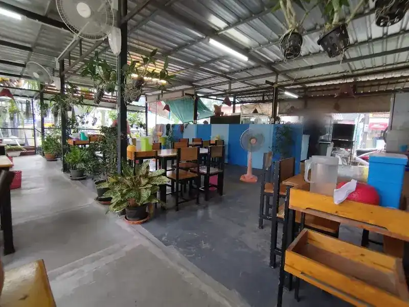 The dining room under a tin roof, with fans, hanging plants and wooden tables