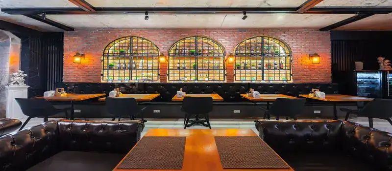 Dining room with a red brick wall, three arched shelves, black leather sofas and wooden tables