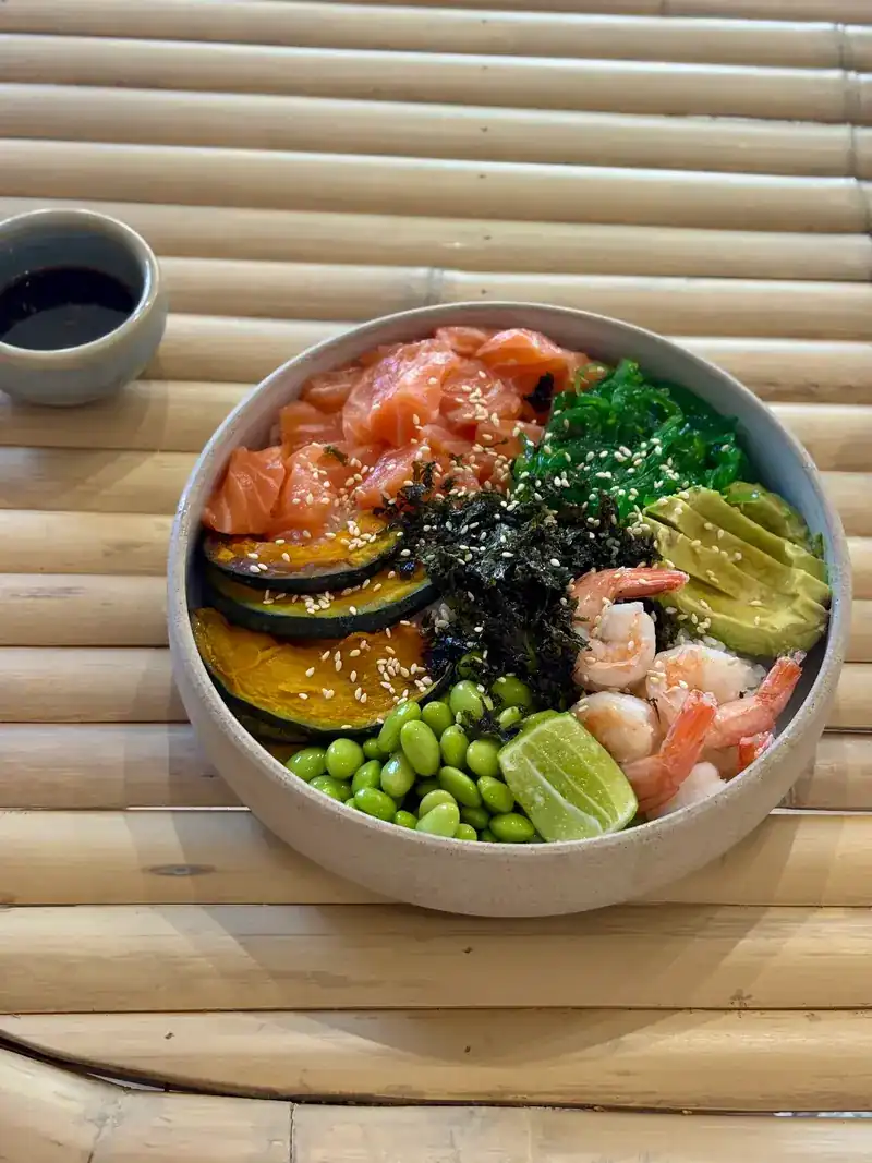 Poke bowl with salmon, prawns, pumpkin, edamame, avocado and seaweed on a bamboo table