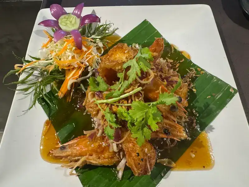 Prawns in a glossy sauce on banana leaf, topped with coriander and a carved onion flower