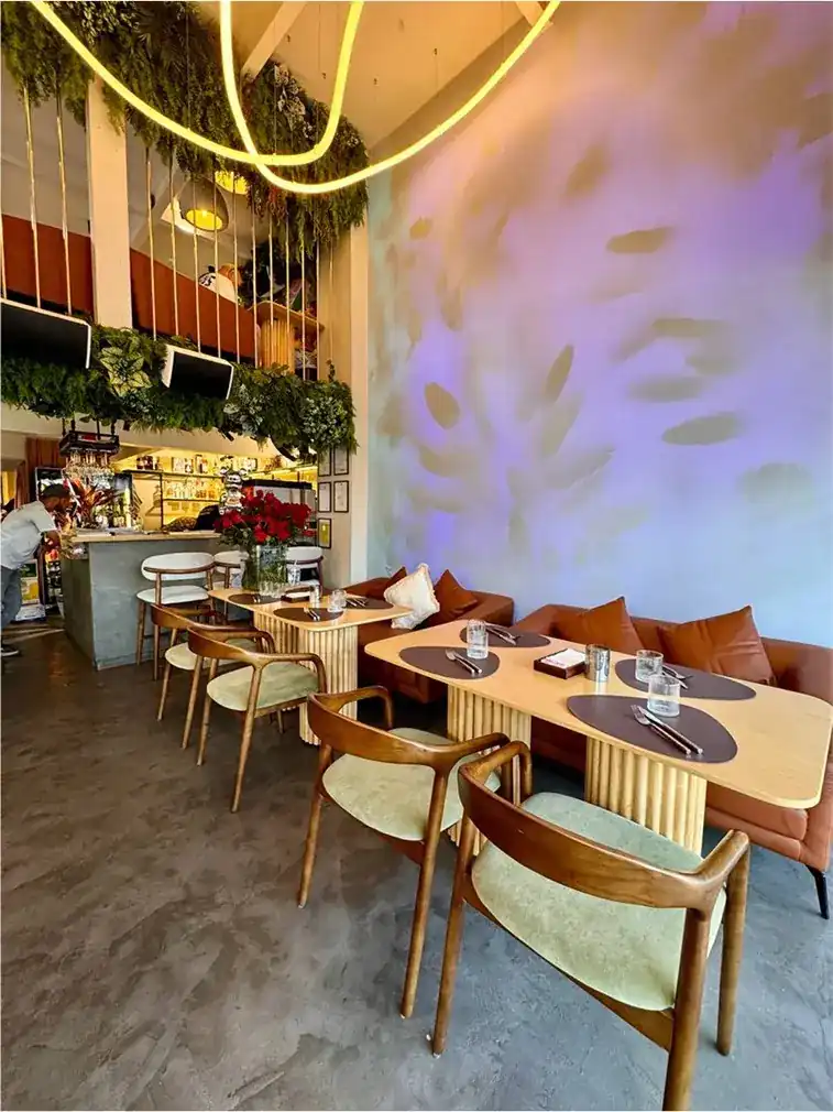 The dining room: pale wood tables, sage chairs and a wall washed in lilac light
