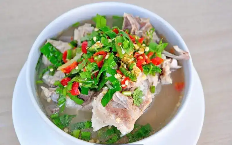 A white bowl of soup with pork, topped with fresh chilli and green herbs