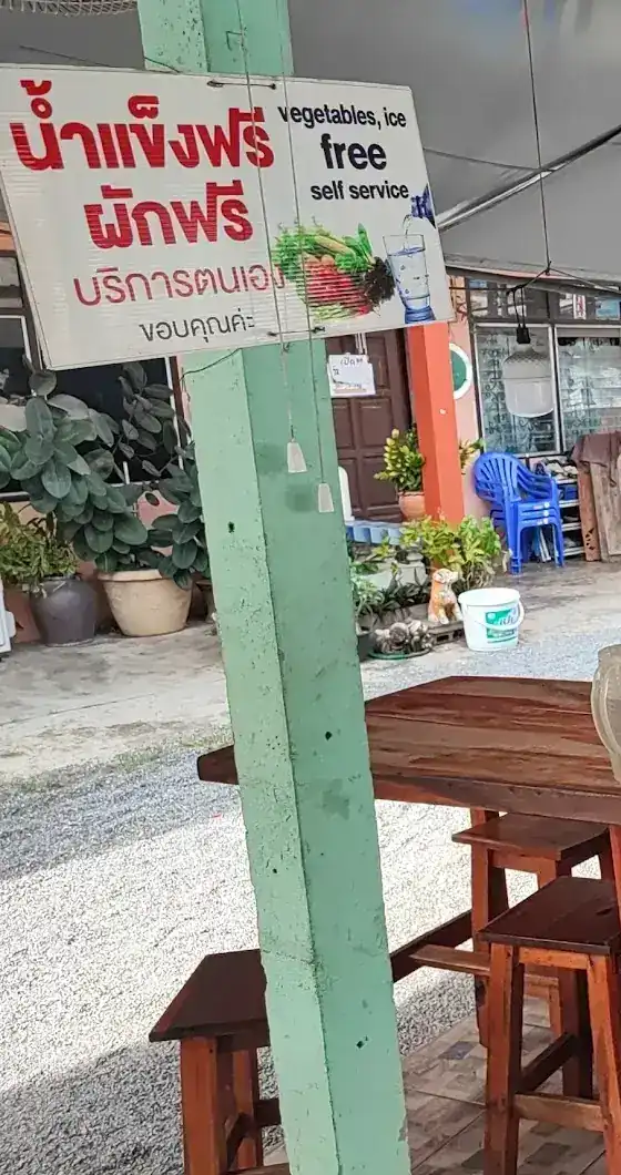 A sign on a green post, free ice and vegetables, self-service, above wooden tables and stools.