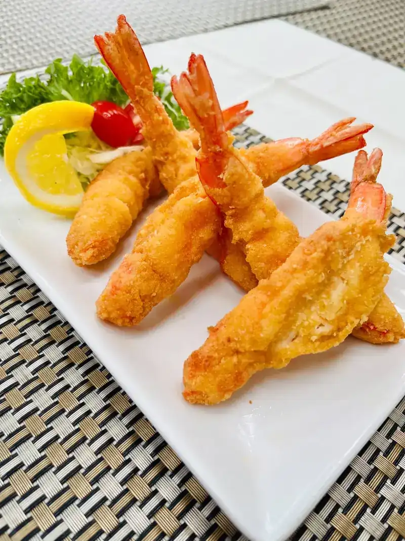 Golden fried prawns on a white plate with lemon and salad
