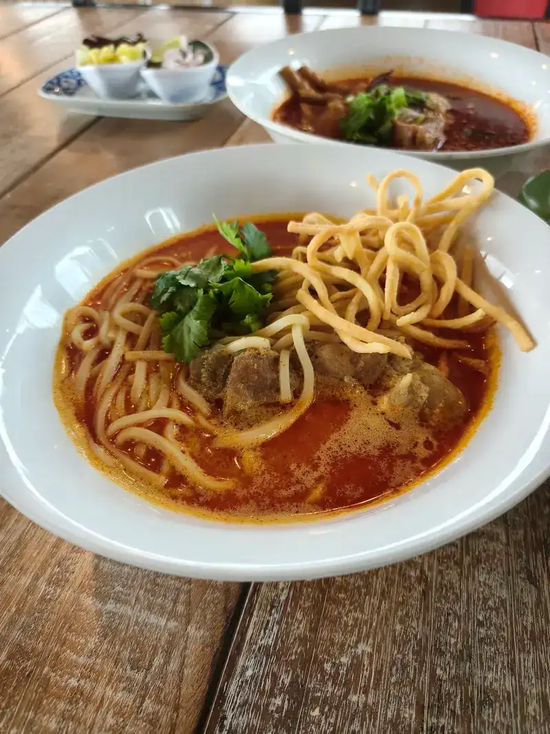 A bowl of khao soi, curry noodle soup topped with crispy noodles and coriander