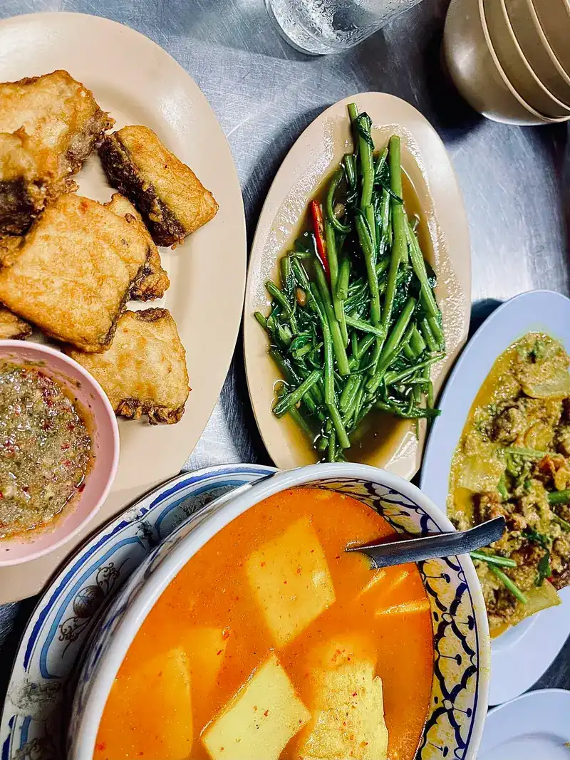 A table of shared dishes: fried pieces, stir-fried morning glory, a chilli dip and an orange curry
