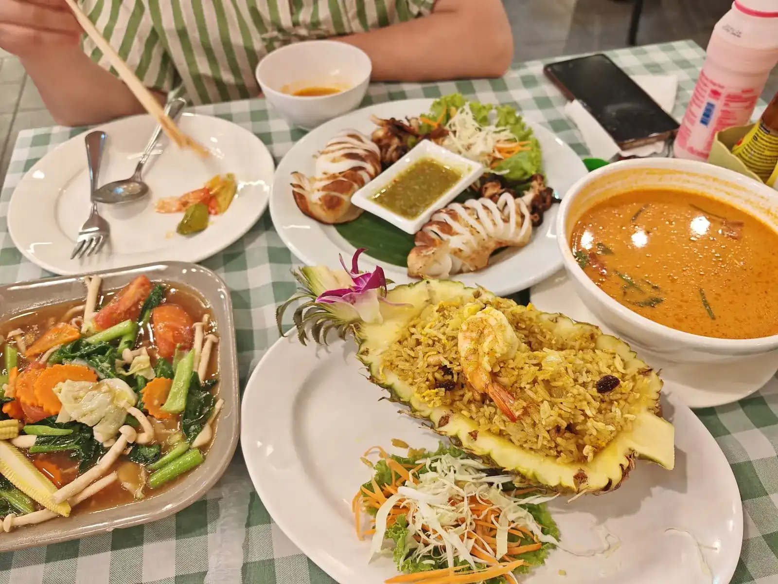 A table at Yoyo: pineapple fried rice with a prawn, grilled squid with dipping sauce, a creamy soup and stir-fried vegetables on a green-check cloth