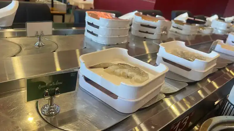 Raw shrimp in white square dishes on the belt, with a name card in front