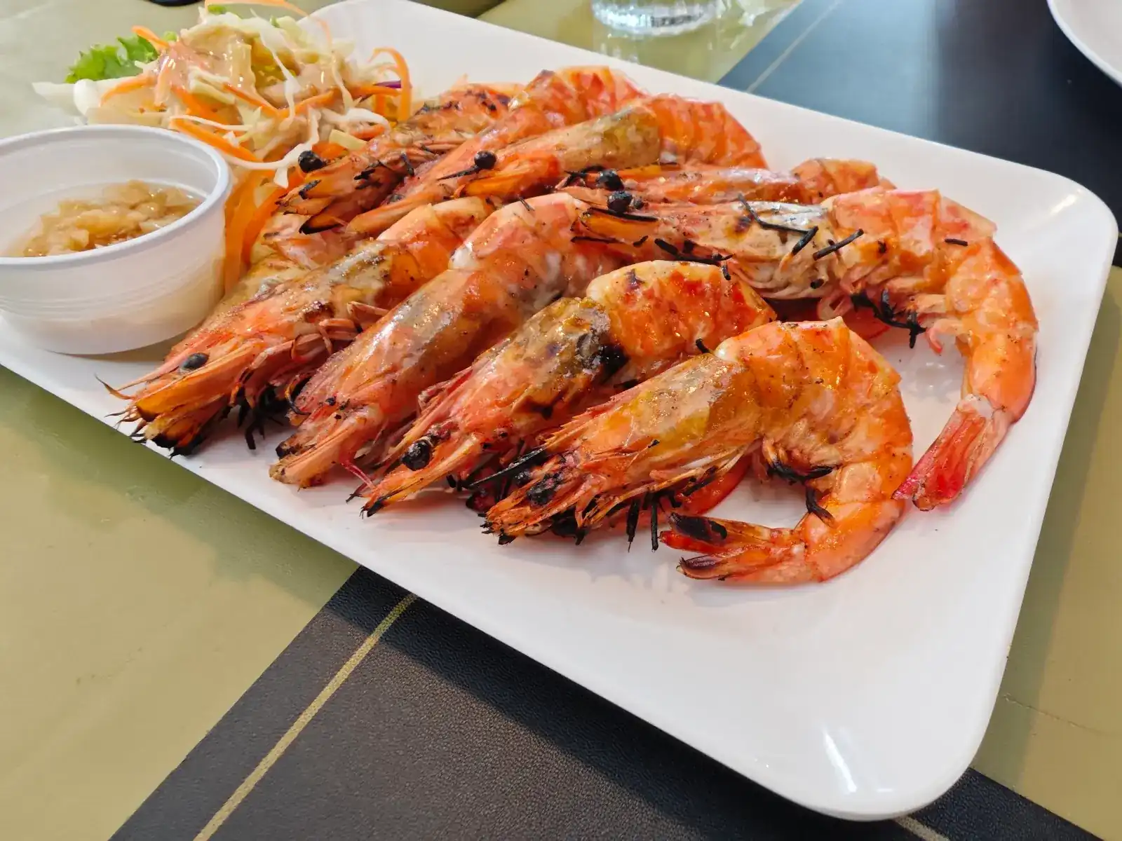 A platter of grilled prawns with salad and a dipping sauce