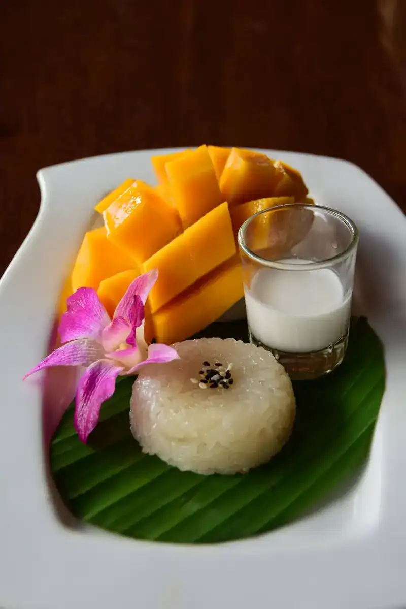 Mango sticky rice on a banana leaf with sliced mango, coconut cream and an orchid