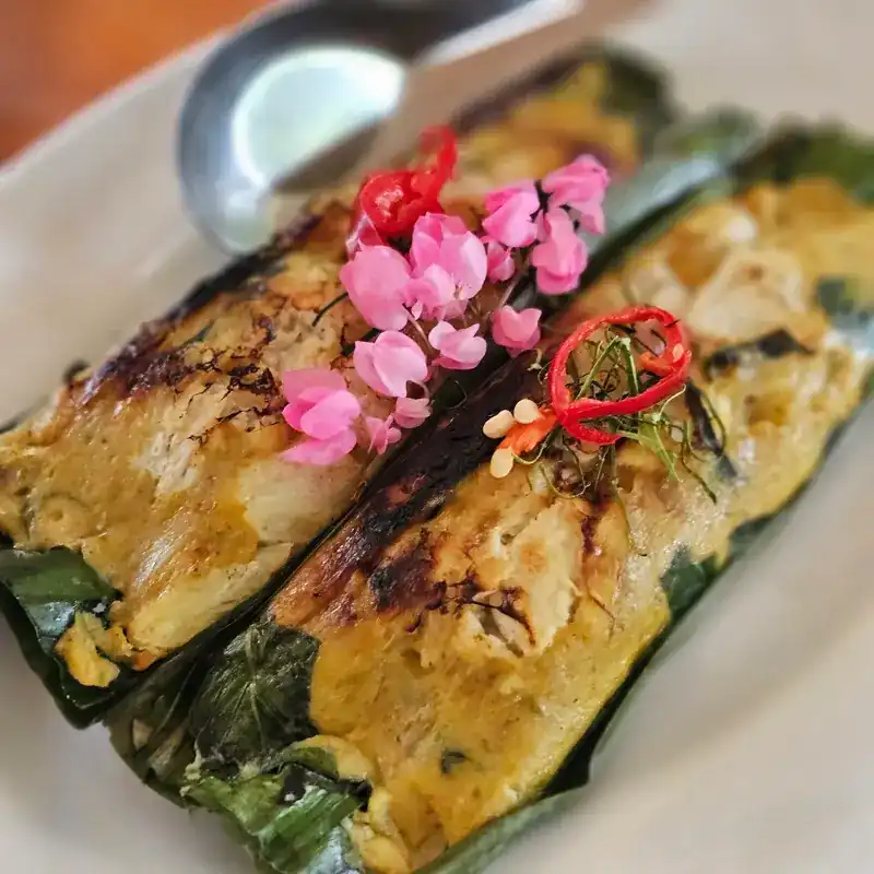 A dish grilled in banana leaf, topped with chilli and pink flowers