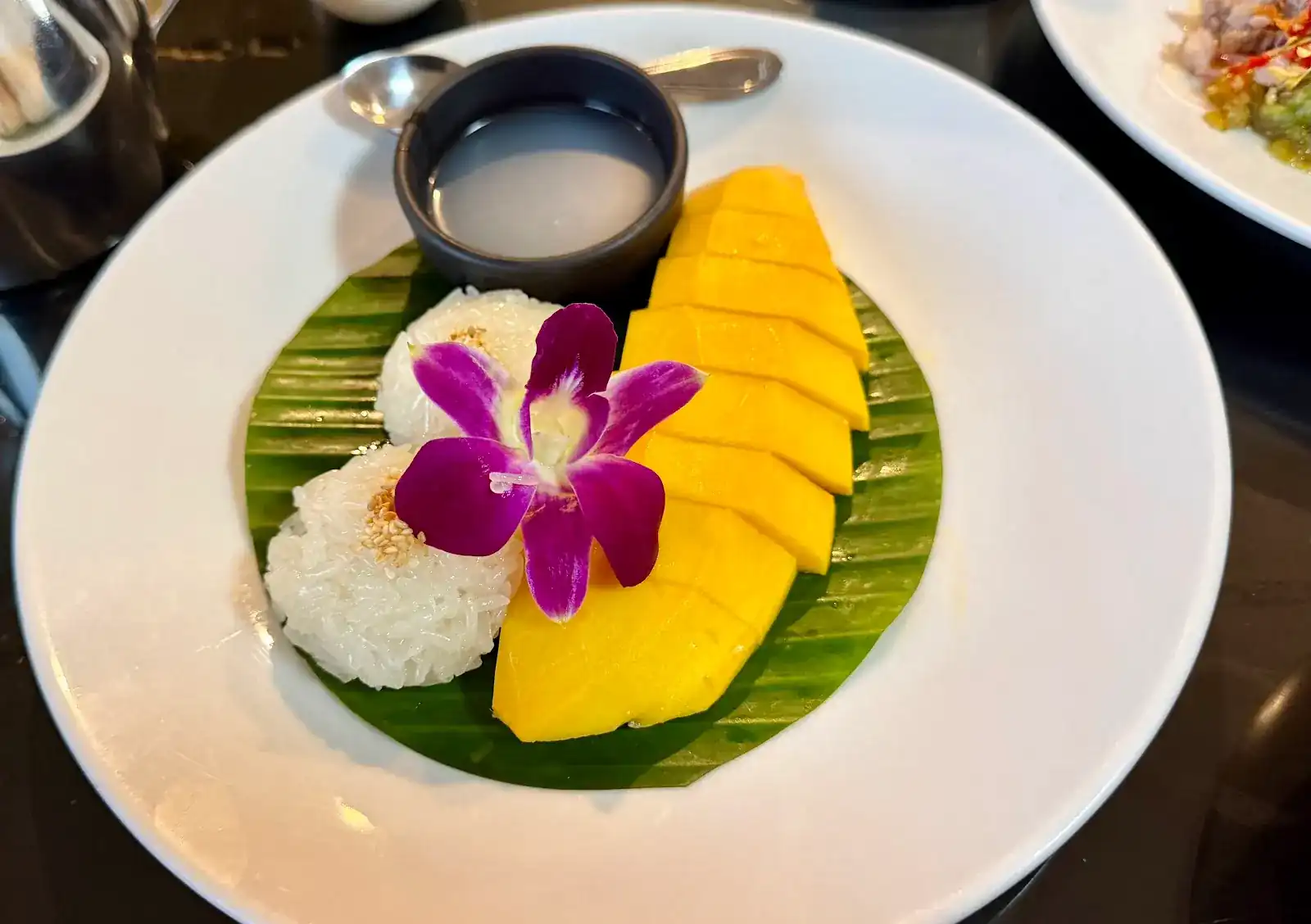 Mango sticky rice on a banana leaf: sliced mango, coconut cream and a purple orchid