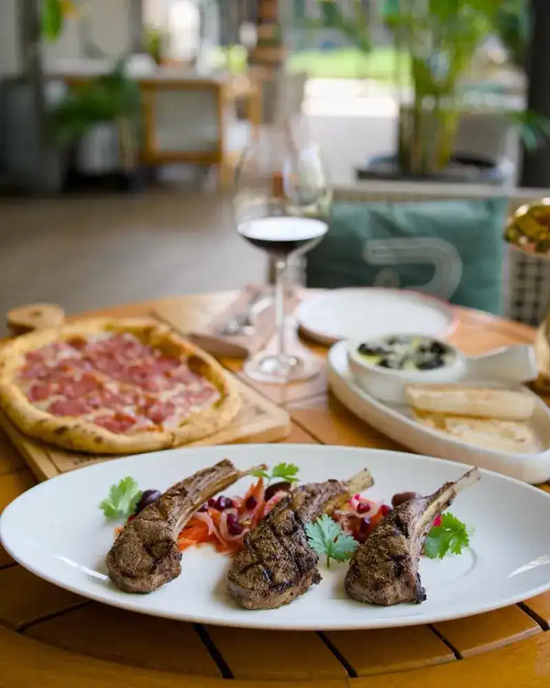 Grilled rack chops with herbs, a salami pizza and a glass of red wine on a terrace table