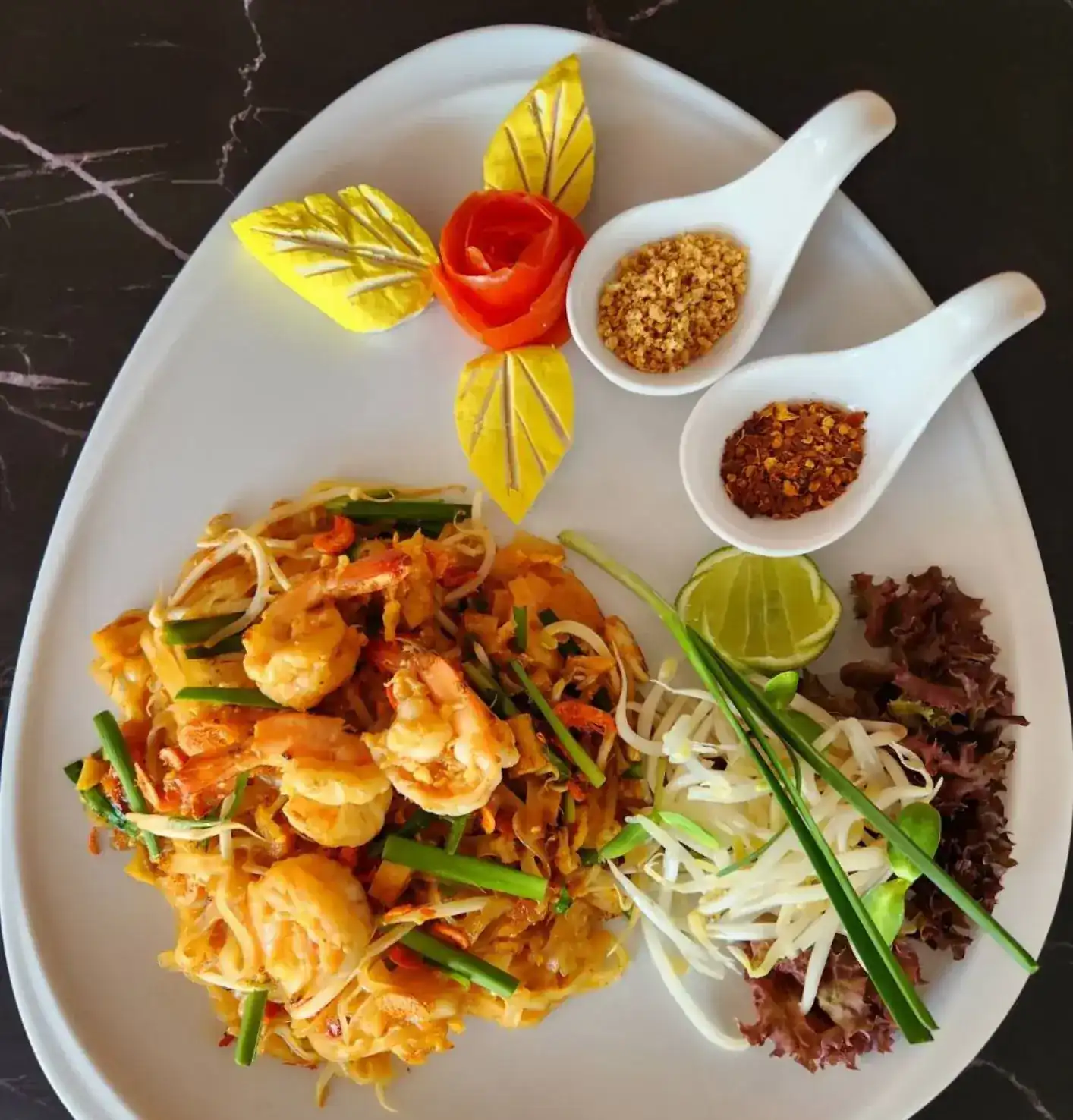Pad Thai with prawns, bean sprouts, lime and carved garnish on a white plate
