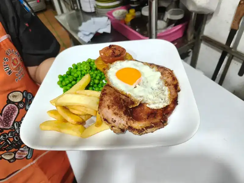 A steak topped with a fried egg, with chips, peas and grilled tomato