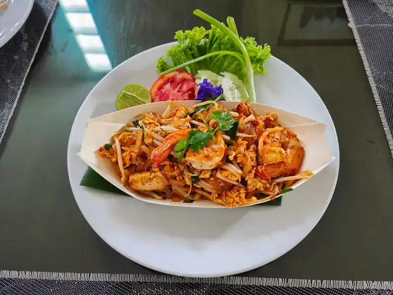 Pad thai with prawns in a paper boat, with lime, tomato and fresh greens