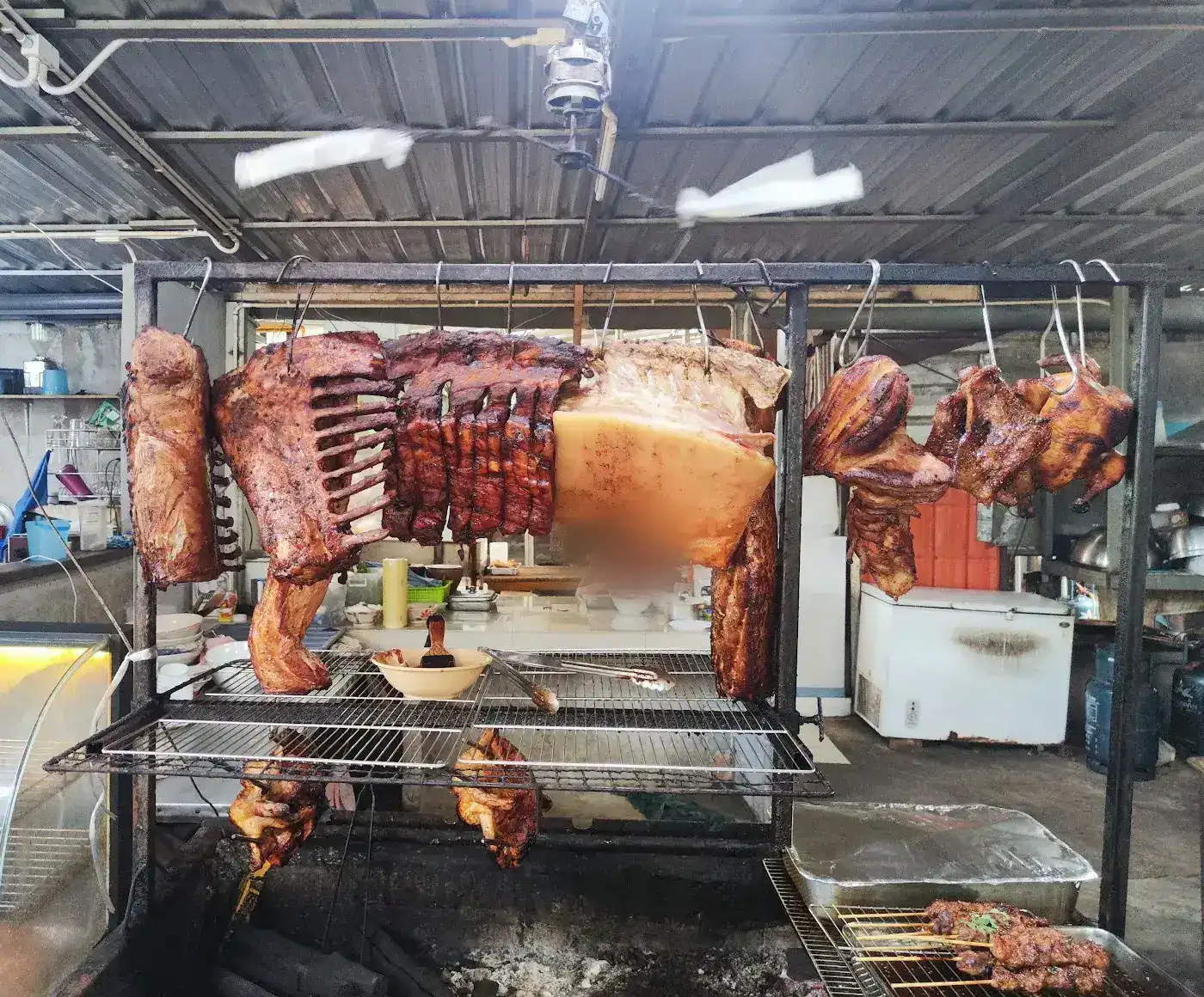 Pork ribs, pork belly and chickens hanging over the charcoal grill