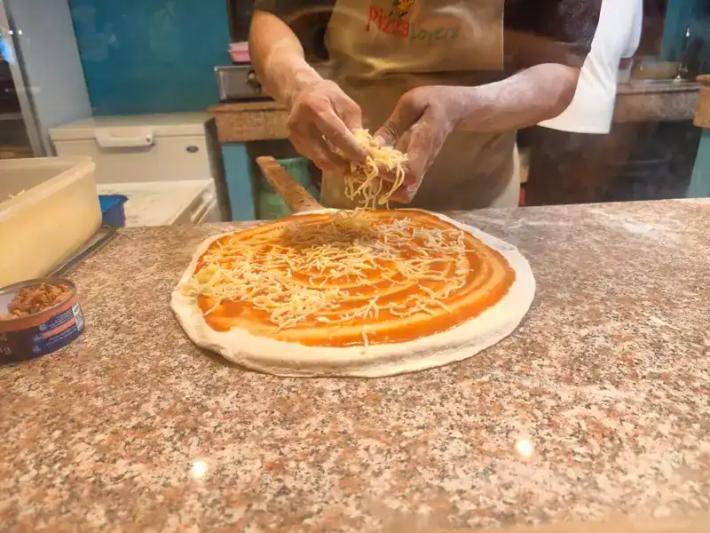 Cheese scattered by hand over a tomato-spread pizza base