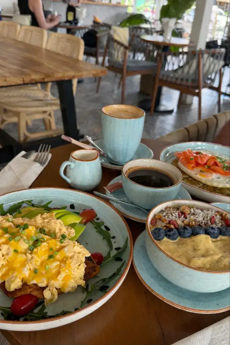 Scrambled eggs with avocado, a smoothie bowl with blueberries and coconut, and two coffees