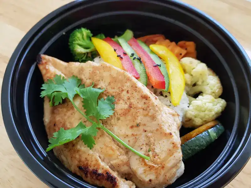 Grilled chicken breast with rice, peppers, broccoli and cauliflower in a takeaway bowl