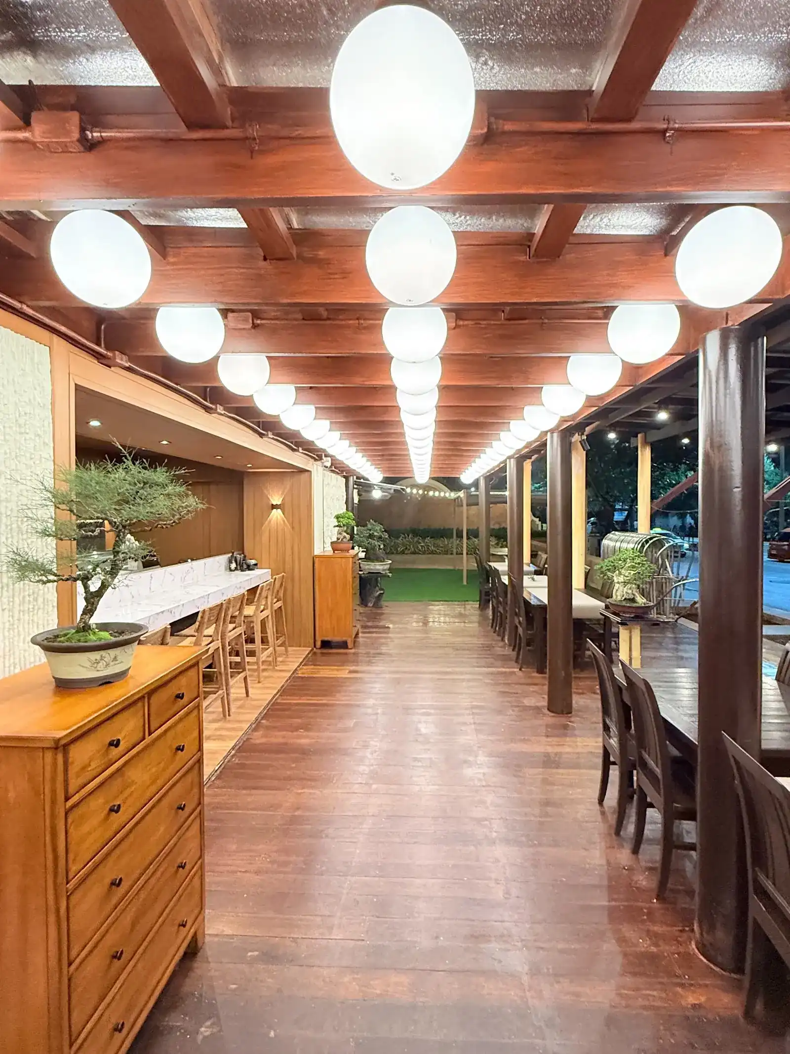 The long wooden hall at Mizuya, lit by rows of round white lanterns, with a bonsai on a dresser