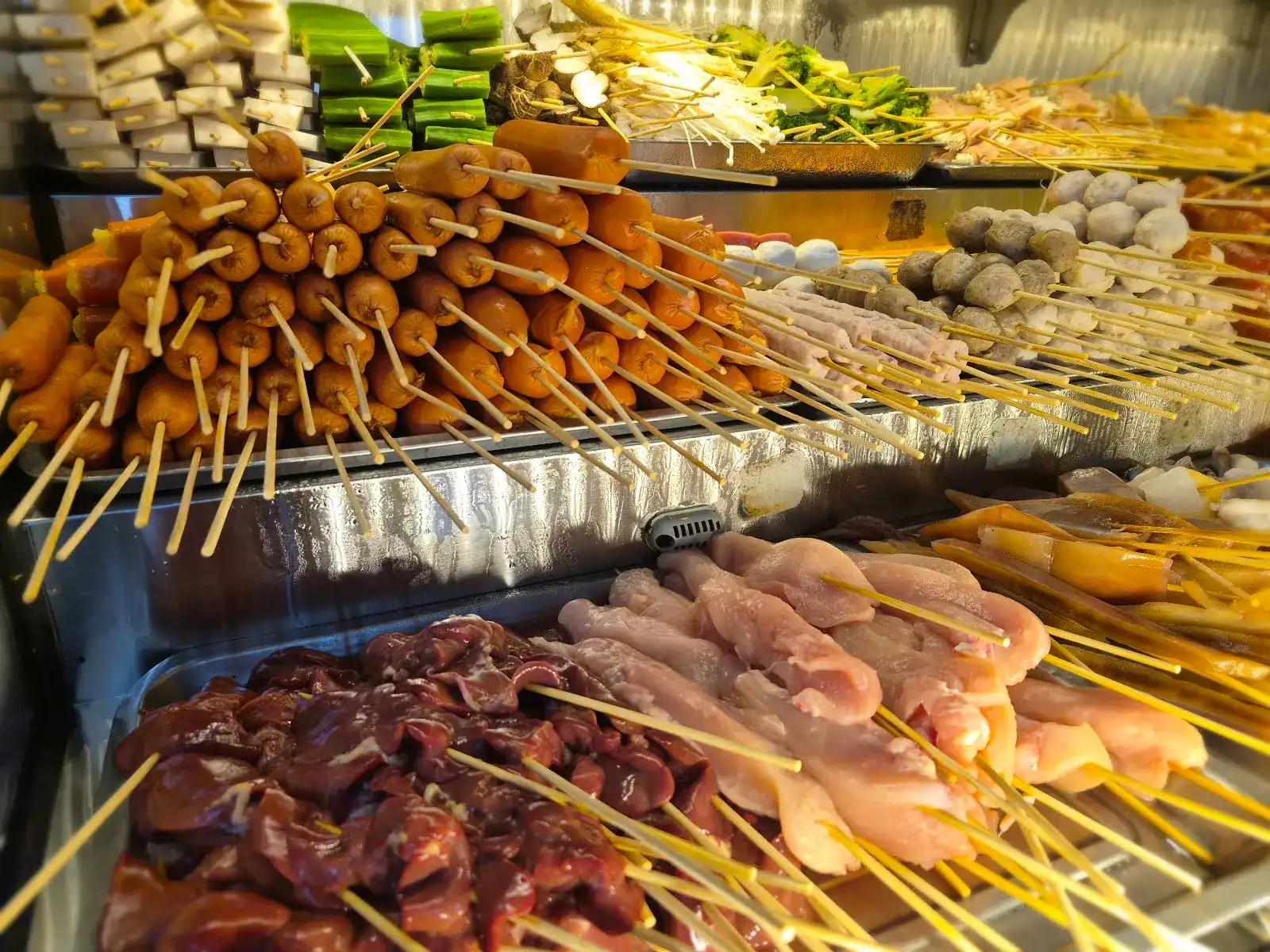 Skewers of sausages, meatballs, chicken and mushrooms in their chiller cabinet