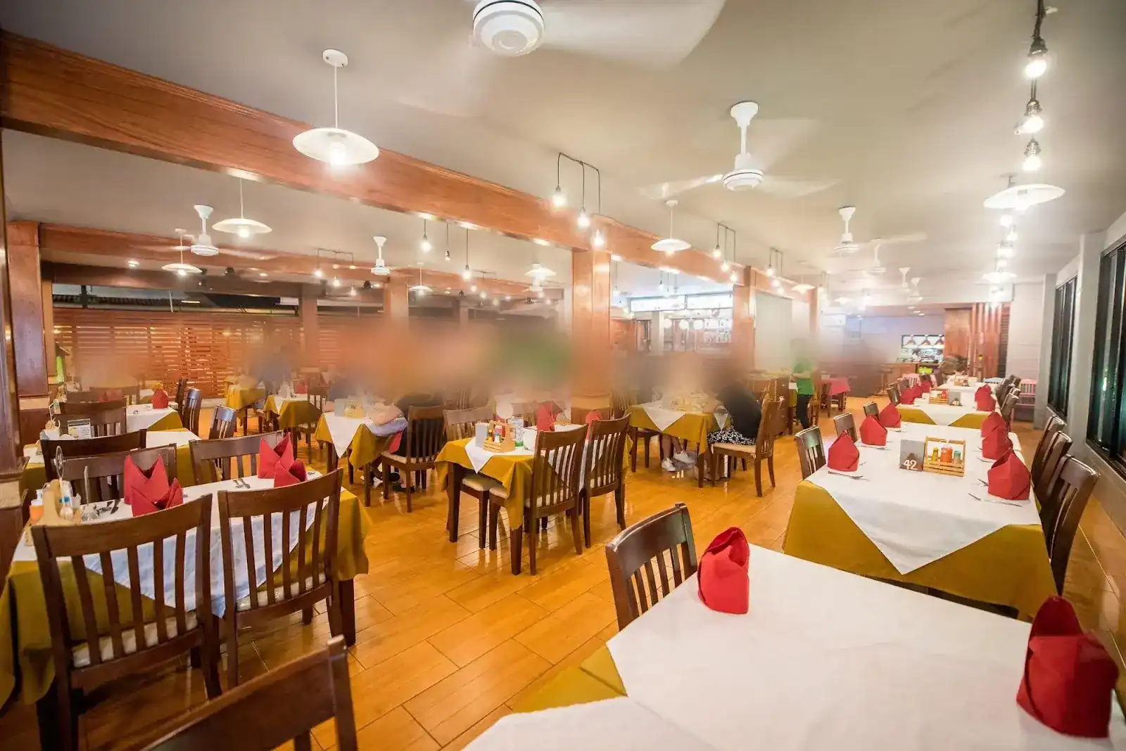 The dining room: wooden pillars, ceiling fans and rows of tables laid with white cloths over gold, with red napkins
