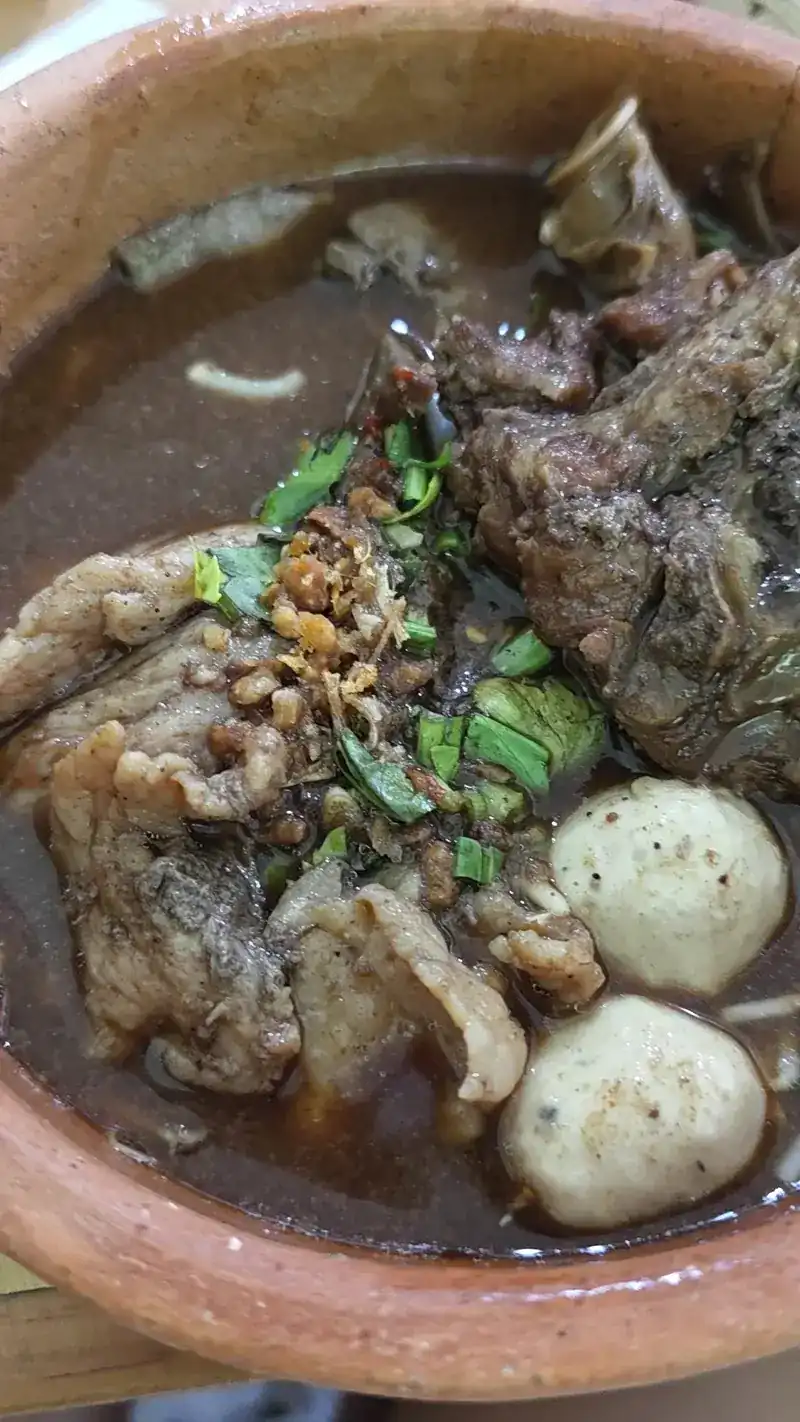 Close-up of boat noodles in the clay pot, with meatballs and herbs