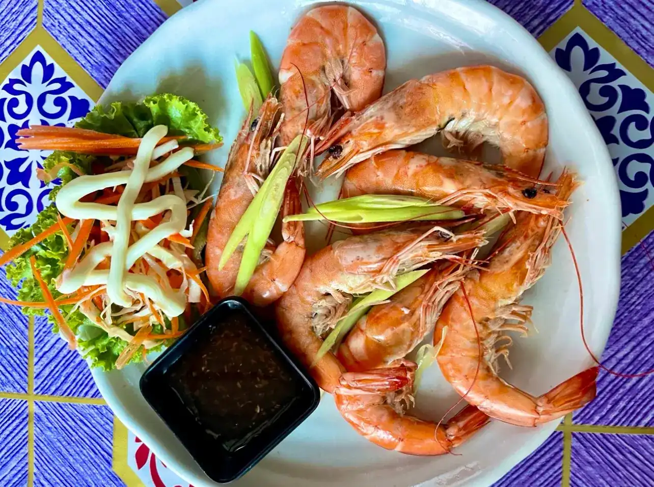 Prawns with a small salad and a dipping sauce, on a blue tile-print tablecloth