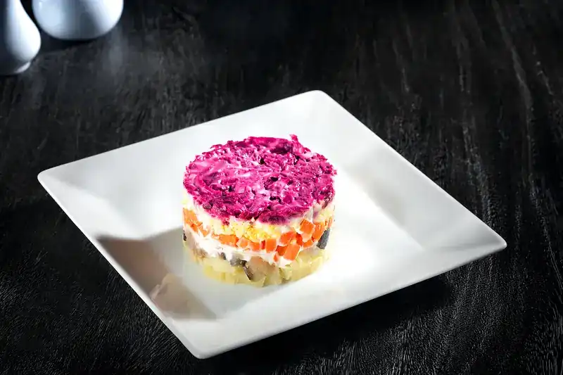A layered salad topped with grated beetroot on a square white plate
