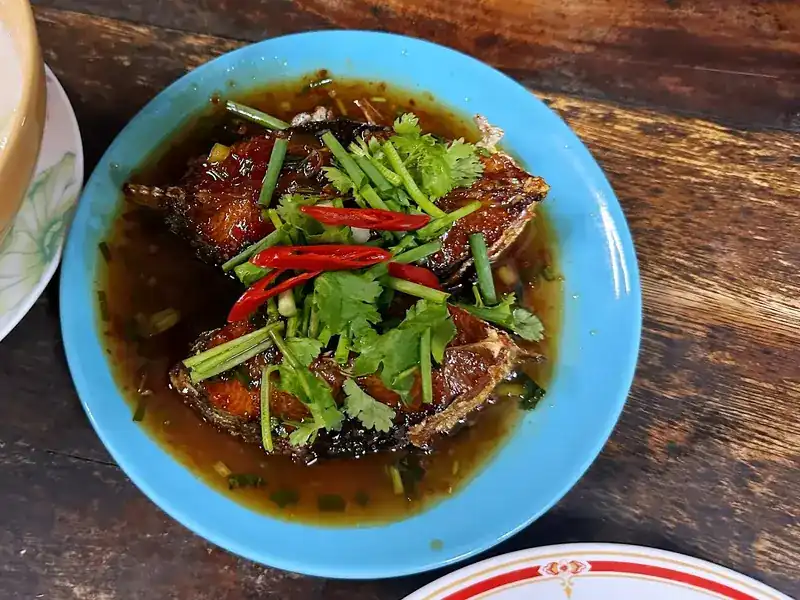 Fried fish in a dark sauce, topped with red chilli, coriander and spring onion, on a blue plate
