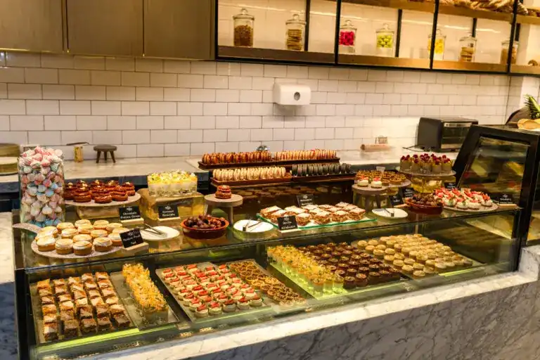 The deli counter filled with macarons, tarts and small cakes against white tiles