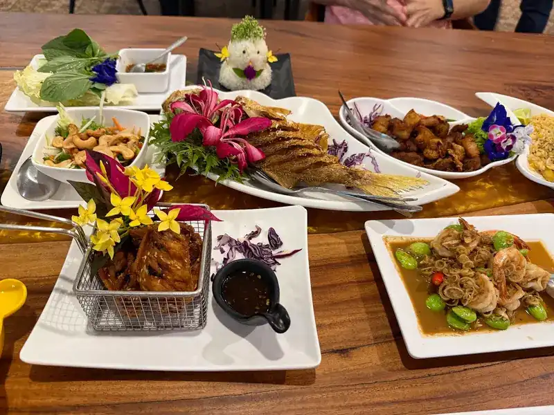 Several dishes on a wooden table, each garnished with flowers, among them prawns with stink beans