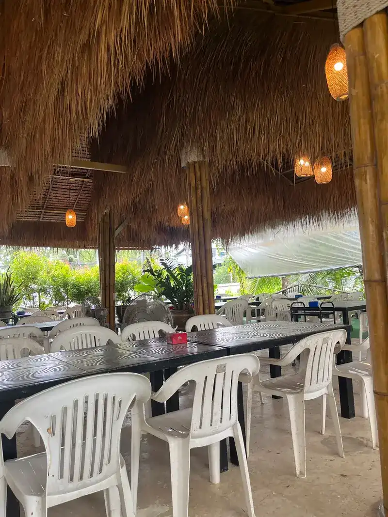 Long tables and white chairs under a thatched roof with woven lamps