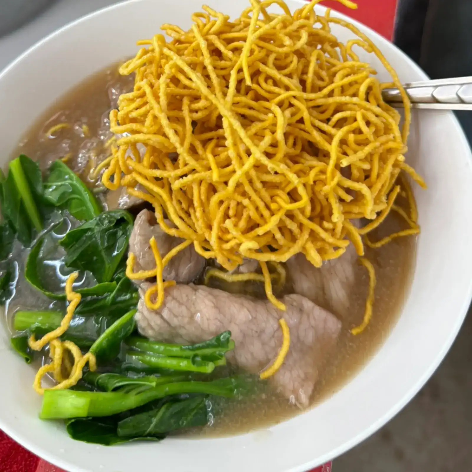 Crispy egg noodles piled on sliced pork and Chinese kale in a bowl of gravy / บะหมี่กรอบวางบนหมูสไลซ์และผักคะน้าในชามน้ำราด
