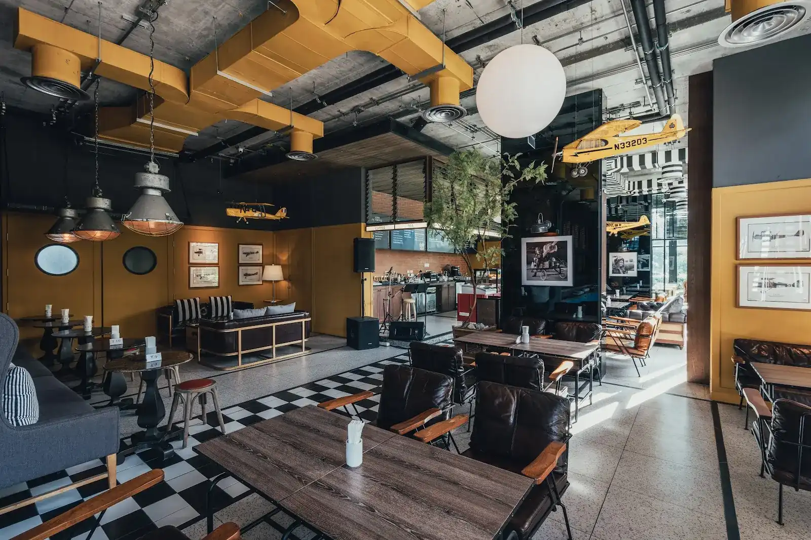 The Midway dining room: yellow ducts, a yellow plane hanging from the ceiling, leather chairs and a checkerboard floor