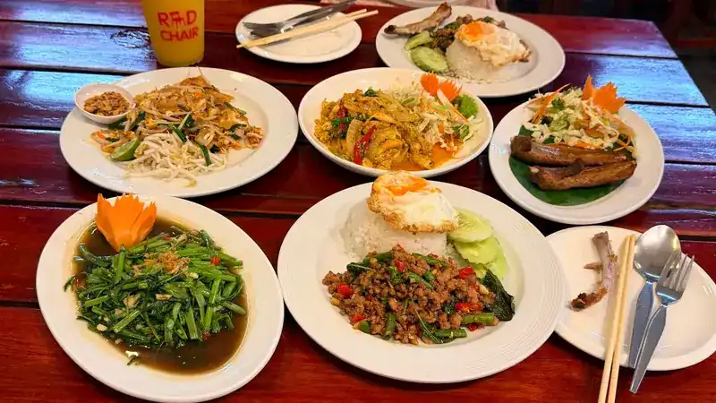 Noodles, stir-fried morning glory and a basil stir-fry on rice with a fried egg, on a red wooden table