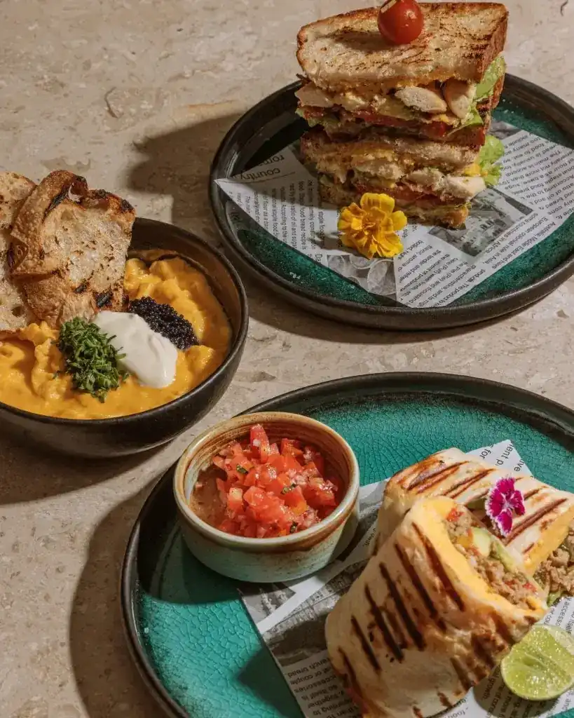 Soft-scrambled eggs with sourdough, the Artis Club sandwich and a breakfast burrito on teal plates