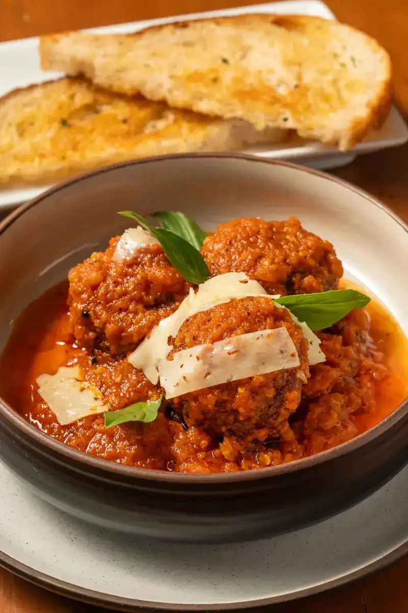 Wagyu beef meatballs in tomato gravy with shaved parmesan and basil, garlic bread behind