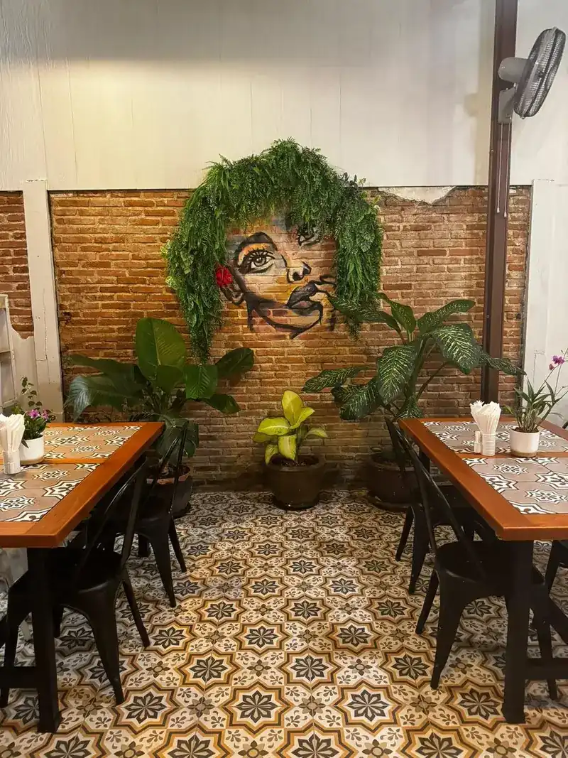 Covered garden with a brick wall, a painted mural framed by ferns, plants and patterned floor tiles