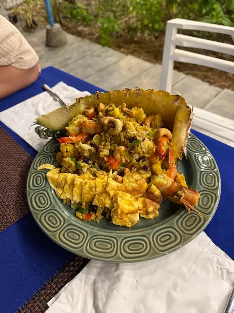 Fried rice served in half a pineapple, with prawns and egg, on a green glazed plate