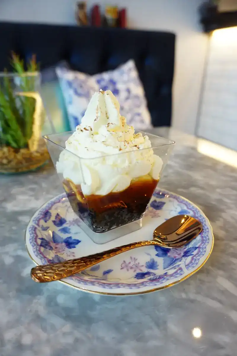 A layered dessert in a glass, topped with cream, on a blue-and-white saucer