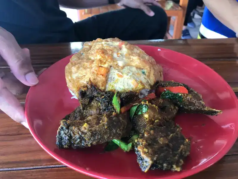 A made-to-order plate of crisp fried pieces with herbs and red chilli, beside a Thai omelette on rice