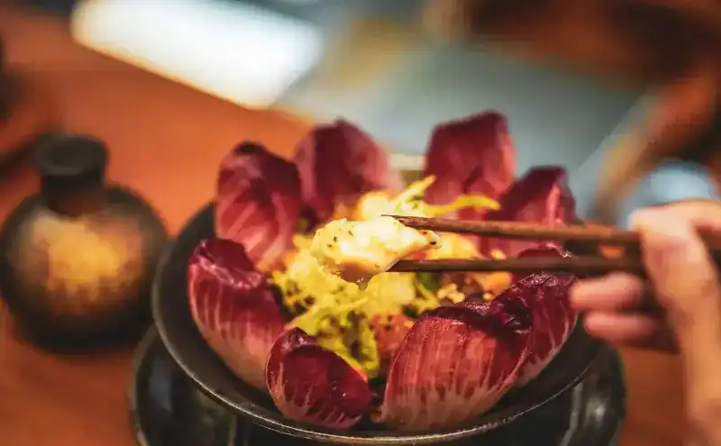 Chopsticks lifting a bite from a bowl ringed with red chicory leaves