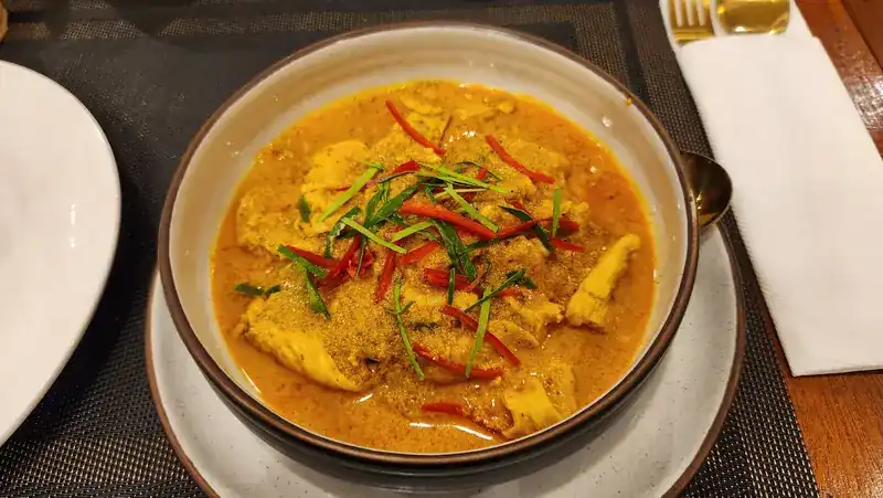 A yellow curry topped with slivers of red chilli and herbs