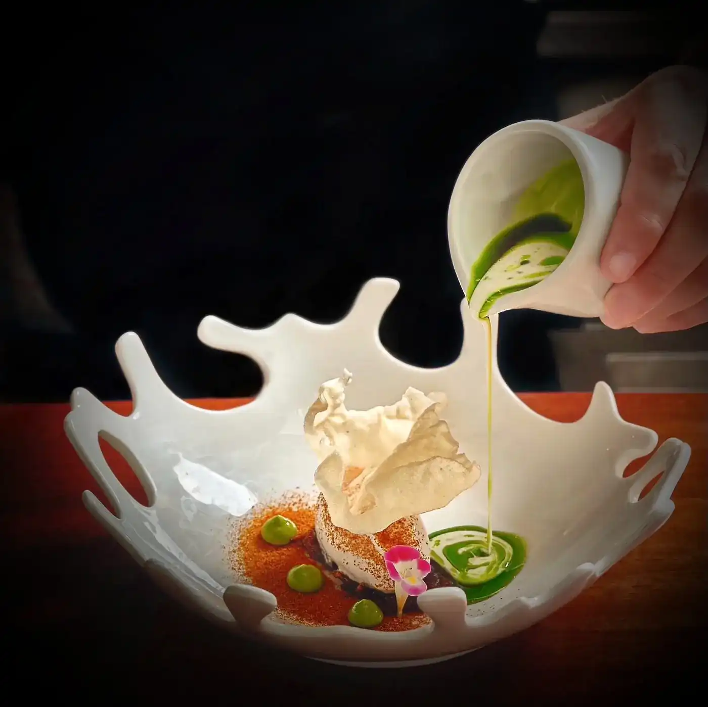 A green sauce poured over a dish in a white porcelain bowl shaped like a splash