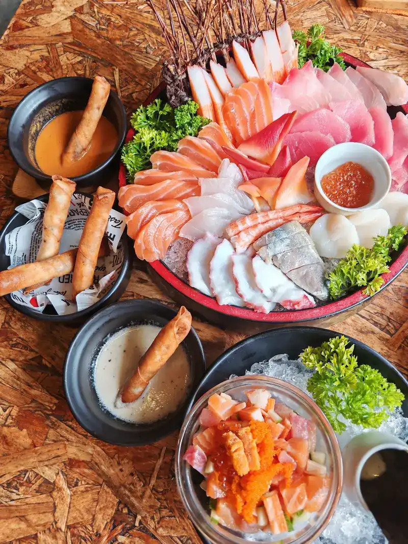 A sashimi platter seen from above, with salmon, tuna, white fish, octopus and prawn, beside fried rolls and dipping sauces