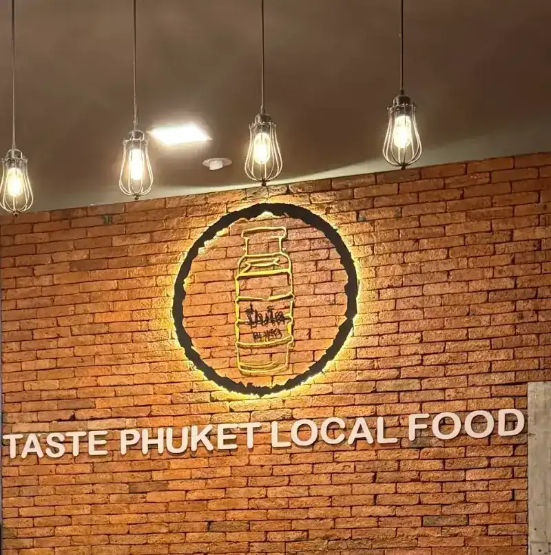 The brick wall inside, with the lit pinto sign above the words Taste Phuket Local Food