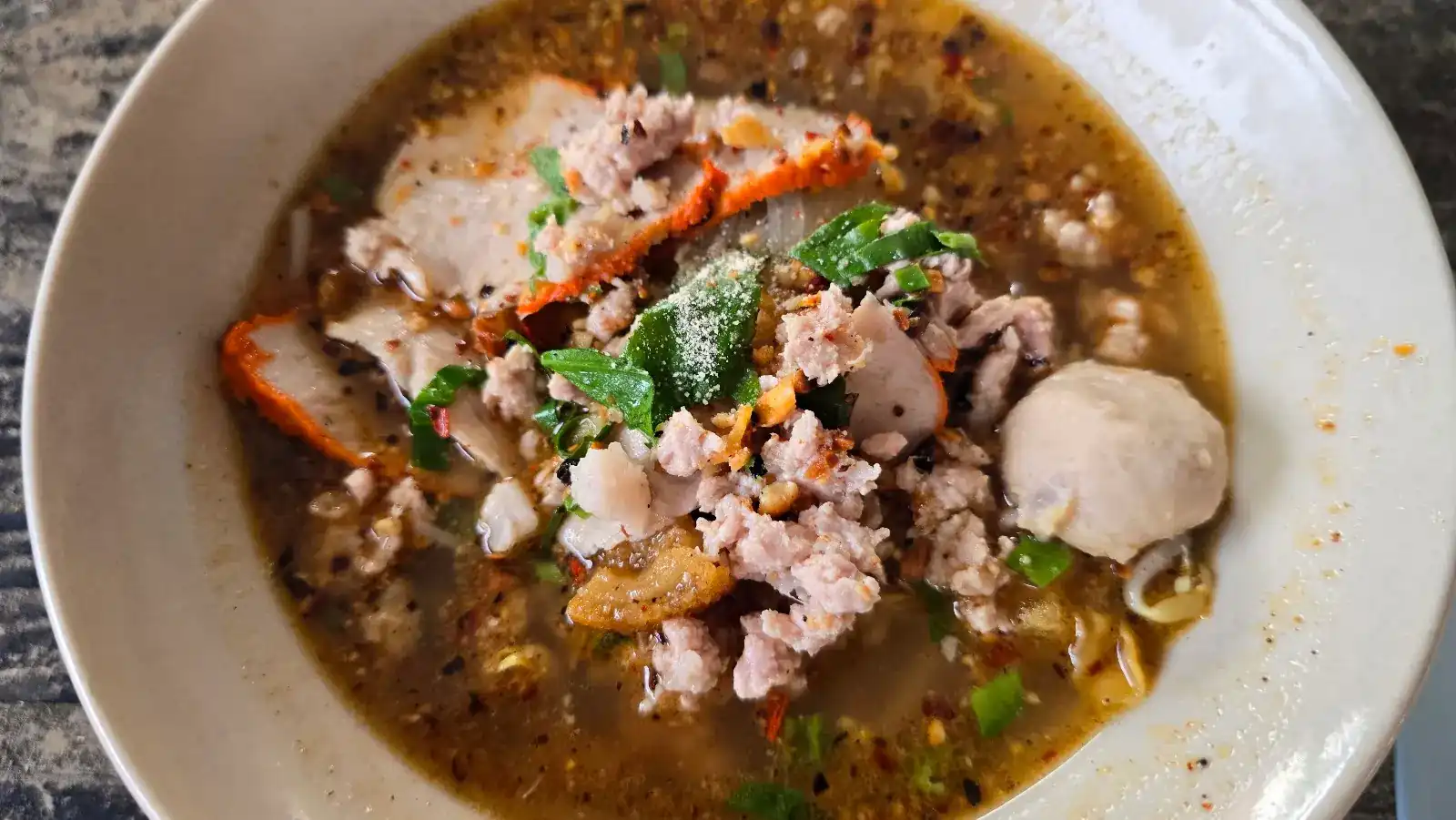 A bowl of Sukhothai noodles in soup with red pork, minced pork, a pork ball and chilli / ก๋วยเตี๋ยวสุโขทัยน้ำ ใส่หมูแดง หมูสับ ลูกชิ้น และพริก